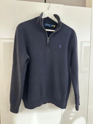 Marinblå halvzip från Polo Ralph Lauren - Klassisk marinblå tröja från Polo Ralph Lauren med halvzip och ståkrage. Tröjan har lång ärm. Och den ikoniska broderade loggan på bröstet. Perfekt för en stilren och avslappnad look. priset kan diskuteras om