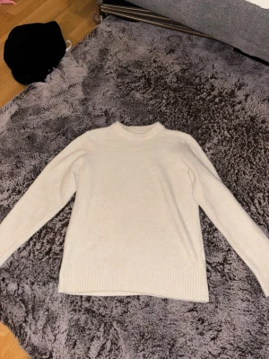 Beige stickad tröja med rund hals - En stilren beige stickad tröja med rund halsringning och långa ärmar. Tröjan har ribbstickade muddar vid ärmslut och nederkant, vilket ger en klassisk och enkel look. Perfekt att matcha med jeans eller kjol.