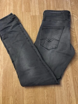 Gråa replay jeans Anbass W29 L32 - Snygga grå jeans med raka ben och klassisk femficksdesign. Jeansen har en diskret tvättad look och stilrena sömmar på bakfickan. Perfekta för dig som gillar en enkel och stilren vibe.