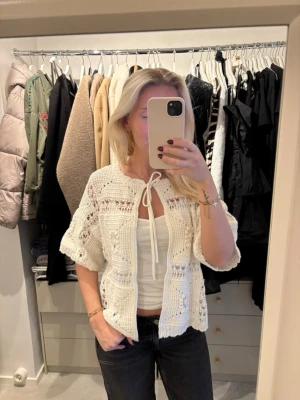 Vit virkad kofta med knytband -  vit virkad kofta med kort ärm och knytband framtill. Koftan har ett luftigt, mönstrat virkade partier 