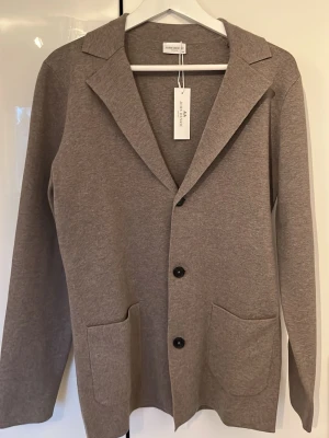 Beige stickad kavaj från John Henric - Stilren beige stickad kavaj från John Henric med klassisk krage, tre knappar framtill och två stora fickor. Kavajen är långärmad och har en mjuk, stickad känsla som passar perfekt till lager på lager. Enkel och snygg design som funkar till det mesta. Inte använd en enda gång och prislapp kvar. Nypris: 1000 kr. Priset kan diskuteras 