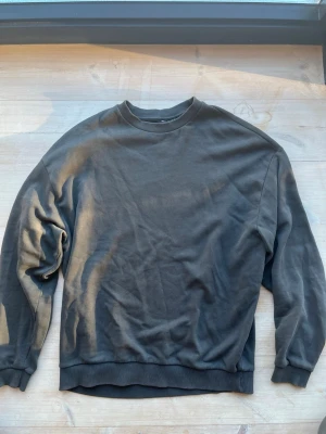 Mörkgrå sweatshirt från ASOS DESIGN strl L - En enkel och stilren mörkgrå sweatshirt från ASOS DESIGN. Tröjan har rund halsringning, ribbade muddar vid ärmslut och nederkant samt en avslappnad passform. Tillverkad i mjukt bomullsmaterial som känns skönt mot huden.