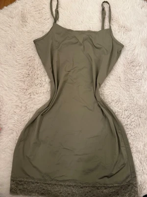 Olivgrönt nattlinne med spetskant - Olivgrönt nattlinne med smala axelband och rak passform. Nedtill finns en dekorativ spetskant som ger en extra fin detalj. Mjukt och lätt material som känns skönt mot huden. Perfekt för mysiga kvällar hemma.