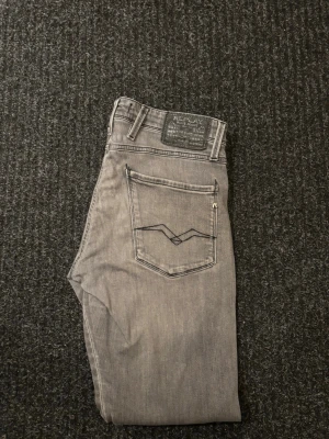 Replay anbass jeans - Säljer ett par gråa Replay jeans i storlek w32/l32 med klassisk femficksdesign. Jeansen har snygga detaljer på bakfickorna och en svart Replay-patch i midjan. Materialet är mjukt jeans-tyg och färgen är ljusgrå med lite tvättad look.
