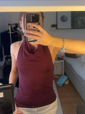 Vinröd halterneck linnetopp - Säljer en vinröd halterneck topp med hög hals och öppen rygg. Toppen är figurnära och ärmlös, perfekt för varma dagar eller när du vill ha en clean och enkel look. Materialet känns mjukt och stretchigt, troligen bomull eller polyester. Är i ett super bra skick🥰