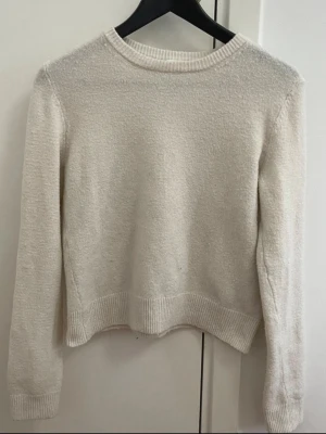 Vit stickad tröja från H&M - En enkel och stilren vit stickad tröja från H&M i storlek S. Tröjan har rund halsringning, ribbade muddar vid ärmslut och nederkant samt lång ärm. Perfekt att matcha med jeans eller kjol för en clean look.