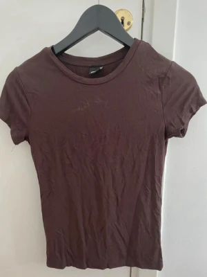 Brun basic t-shirt från Gina Tricot - En enkel brun t-shirt från Gina Tricot i storlek S. Modellen är klassisk med rund halsringning och korta ärmar. Tillverkad i mjuk bomull som känns skön mot huden. Perfekt att matcha med jeans eller kjol för en clean look.