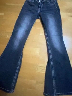 Bootcut jeans från Gina Tricot - Säljer ett par mörkgrå bootcut jeans från Gina Tricot i storlek 164. Jeansen har vita kontrastsömmar, klassiska fickor och är tillverkade i ett mjukt jeansmaterial. Snyggt utsvängda ben och cool tvätt framtill.