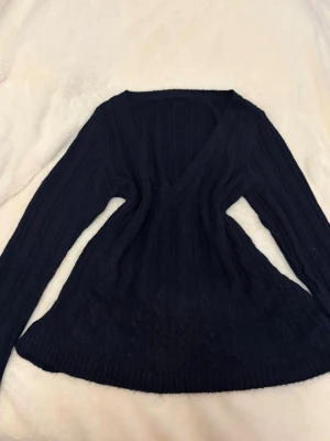 Långärmad mörkblå babydoll topp - Mysig mörkblå stickad tröja med v-ringning och lång ärm. Tröjan har ribbade detaljer längs hela plagget och en figurnära passform som framhäver midjan. Perfekt för kyligare dagar och enkel att styla med jeans eller kjol. (Allting tvättas innan leverans)