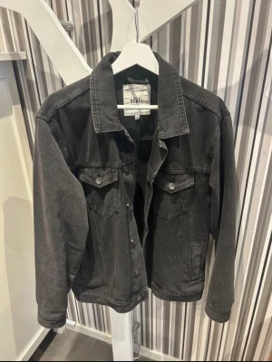 Svart jeansjacka från REBEL - Säljer en svart jeansjacka från REBEL i klassisk modell med knappar framtill och två bröstfickor med lock. Jackan har en rak passform och långa ärmar. Perfekt att slänga över en hoodie eller t-shirt för en chill look. Säljer då jag ej använder den längre, hör av er för fler frågor😊