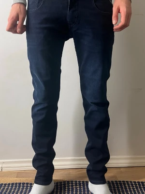 Mörkblå replay - Säljer ett par mörkblå skinny jeans med klassisk femficksdesign och smal passform. Jeansen har en snygg tvätt och sitter tight hela vägen ner. Perfekta för dig som gillar en stilren och modern look.