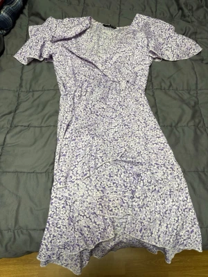 Ljuslila blommig klänning från SHEIN - Supersöt kortklänning från SHEIN i ljuslila och vitt med blommigt mönster. Klänningen har volangdetaljer, v-ringning och korta ärmar. Det kommer med ett bälte/snöre med också så man kan knyta 