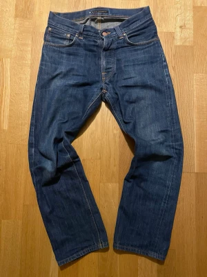 Nudie Jeans Loose Leif W27 L30 blå - Säljer ett par Nudie Jeans Loose Leif i modellen Dry Authentique. De är blå, sitter i regular fit och är gjorda av 100% ekologisk bomull. Klassisk femficksdesign och snygga kontrastsömmar. Perfekta om du gillar en avslappnad och vanlig stil. Tveka inte på att fråga!