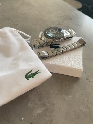 En lacost armband och Hugo boss klocka  - Bilderna visar en klocka och tillbehör från Lacoste, men ingen väst syns på någon av bilderna.