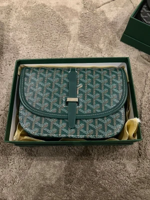 Grön mönstrad axelväska  - Säljer en grön axelväska med ikoniskt grafiskt mönster och snyggt spänne framtill. Väskan har en klassisk form och detaljer i skinn, perfekt för dig som vill ha något unikt och stilrent. Levereras i originalkartong.