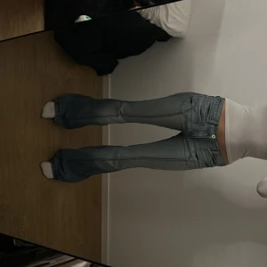 Ljusblå bootcut jeans lågmidjade - Säljer ett par ljusblå bootcut jeans med låg midja och klassiska fem fickor. Jeansen har slitningar och markerade sömmar längs benen för en extra cool vibe. Perfekta för dig som gillar retrostil och vill ha ett par jeans som sticker ut.