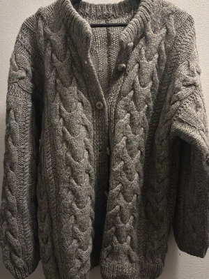Grå handstickad kofta med flätmönster - Mysig grå stickad kofta med grovt flätmönster och stora knappar framtill.  Ca M/L