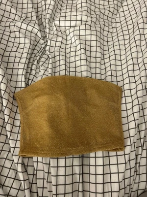 Guldig glittrig bandeau topp H&M XS - Säljer en guldig bandeau topp från H&M i storlek XS. Toppen är glittrig och axelbandslös med en mjuk insida för extra komfort. Perfekt för dig som vill sticka ut med en snygg och trendig look.