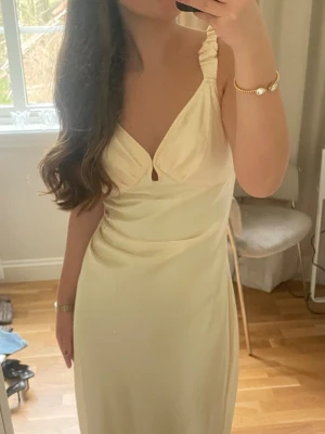 Gul siden klänning från Adoore  - Använt endast 1 gång!!! Säljer en elegant ljus långklänning med v-ringning och smala axelband med rynkdetalj. Klänningen har en mjuk, följsam passform och ett litet nyckelhålsutskärning framtill. 