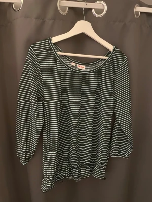 Randig topp från John Baner - Säljer en svart och vit randig topp från John Baner Jeanswear i storlek S. Toppen har trekvartsärm, rund halsringning och resår i nederkanten för en avslappnad passform. Tillverkad i mjuk bomull som känns skön mot huden.