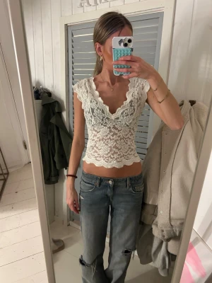 Vit spetsblus från Stradivarius - Supersöt vit blus från Stradivarius i spets med v-ringning och korta ärmar. Croppad modell med fina vågiga kanter och blommigt spetsmönster. Perfekt att styla med jeans eller kjol för en trendig look.