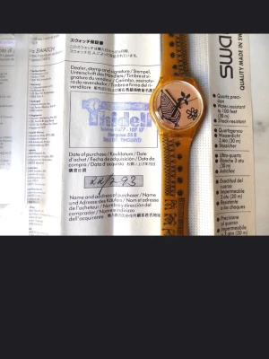 Swatch Nytt batteri.  - Bilderna visar en Swatch-klocka med transparent gul plastarmband och svart grafiskt mönster. 