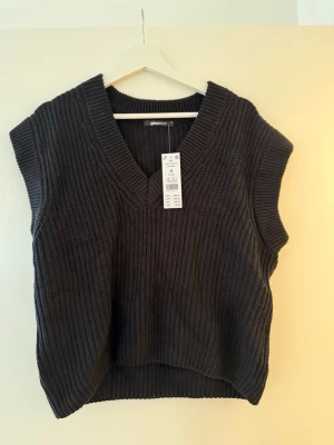 Svart stickad väst från Gina Tricot - Säljer en svart stickad väst från Gina Tricot i storlek M. Västen har bred ribbstickning, djup v-ringning och en relaxed passform. Perfekt att styla över en skjorta eller t-shirt för en trendig lager-på-lager-look.