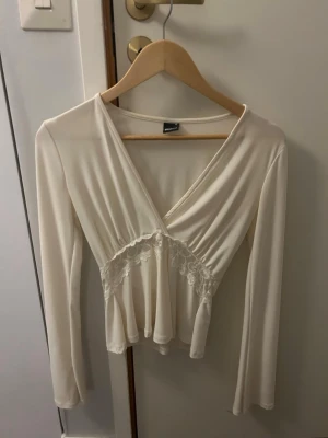 Vit omlottopp med spetsdetalj - Säljer en vit omlottopp från Gina Tricot med långa ärmar och v-ringning. Toppen har fina spetsdetaljer under bysten och ett lätt, flowy tyg som ger en romantisk känsla. Perfekt att styla med jeans eller kjol för en söt look.