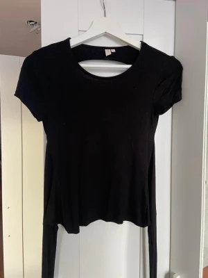 Svart topp med öppen rygg från Nelly - Säljer en svart kortärmad topp från Nelly i storlek XS. Toppen har en rund halsringning, öppen rygg och knytband bak som ger en snygg detalj. Tillverkad i mjukt bomullsmaterial och sitter tight mot kroppen. Perfekt för dig som vill ha en trendig och stilren look.🩷