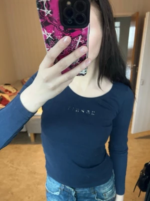 Mörkblå långärmad topp Esprit - Säljer en mörkblå långärmad topp från Esprit med rund halsringning och små glittriga stenar som bildar loggan på bröstet. Toppen är figurnära och gjord i mjukt bomullsmaterial, perfekt till jeans eller kjol.