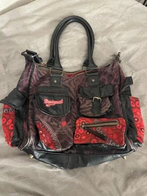 Desigual Sira London Medium Carry bag - Säljer en unik väska från desigual. Den har några hål på nätet på baksidan.