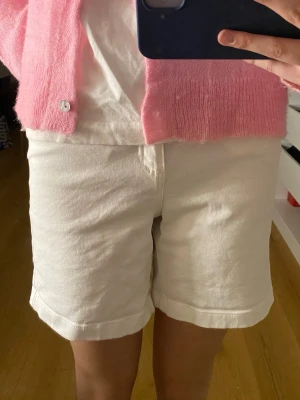 Vita högmidjade shorts från Dobber - Säljer ett par vita högmidjade shorts från Dobber. De har klassisk femficksdesign, raka ben och uppvikta benslut. Materialet är kraftig bomull som ger en clean och fräsch look. Perfekta till sommaren och lätta att matcha med allt.
