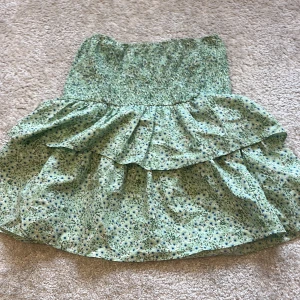 Grön blommig volangkjol Vero Moda XS - Supersöt grön kortkjol från Vero Moda med småblommigt mönster i blått och vitt. Kjolen har smock i midjan och dubbla volanger som ger en riktigt flowy känsla. Perfekt för varma dagar och lätt att matcha med en enkel topp. Kontakta flr fler bilder🩷