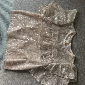 Glitter fest topp - Supersöt fest topp från Lindex i guldigt glitter med fina volanger i ärmarna och vid bröstet  , säljer pga av att den är förliten💕 Använd en gång 