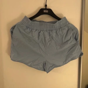 Ljusblå träningsshorts - Snygga ljusblå träningsshorts med elastisk midja och avslappnad passform. Perfekta för gymmet eller löprundan. Materialet är lätt och syntetiskt, vilket gör dem sköna och luftiga under varma dagar.