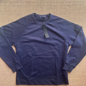 Stone Island sweatshirt - Snygg mörkblå sweatshirt från Stone Island med klassisk rund hals och lång ärm. Tröjan har den ikoniska logotypen på vänster ärm och är gjord i mjuk bomull. Perfekt för dig som gillar stilrena och exklusiva plagg.