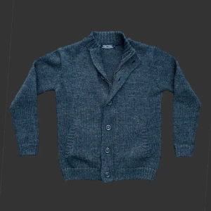 Mörkgrå stickad kofta från Woolovers - Mörkgrå stickad kofta från Woolovers i storlek S. Koftan har ribbad krage, dragkedja och knappar framtill samt två fickor. Materialet är mjuk ull som håller dig varm och stilen är klassisk med långärmade ärmar. Perfekt för kyliga dagar.