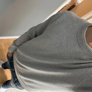 Grå stickad tröja från Björn Borg - Snygg grå stickad tröja från Björn Borg i storlek M. Tröjan har rund hals, ribbade muddar och är långärmad. Perfekt att slänga på sig när det är lite kyligt ute. Enkel och stilren design som funkar till jeans eller andra favoritplagg.