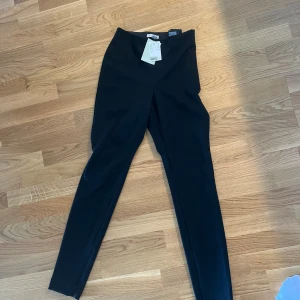 Svarta kostymbyxor med smal passform - Snygga svarta kostymbyxor från Zizzi med hög midja och smal passform. Byxorna har en stilren look utan synliga fickor eller detaljer, perfekta för en clean och modern stil. Materialet är mjukt och stretchigt för extra komfort.