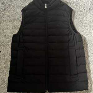 Svart dunväst från Emporio Armani - Säljer en svart dunväst från Emporio Armani Essentials med quiltad design och dragkedja framtill. Storlek är ca XS-S men rekommenderar S. Knappt använd då den är för liten. Nypris ca 3000.