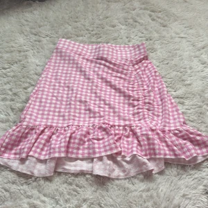 Rutig rosa volangkjol från Gina Tricot - Supersöt kortkjol från Gina Tricot i rosa och vitt rutigt mönster. Kjolen har volangkant nertill och en lätt A-linjeformad passning. Perfekt för dig som gillar en somrig och trendig stil. Tillverkad i mjuk bomull som känns skön mot huden. Säljs inte längre, använt en eller två gånger.