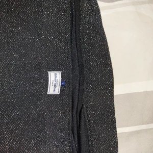 Glittrig svart kortkjol från Croker Apparel - Snygg svart kortkjol från Croker Apparel i storlek L. Kjolen har ett glittrigt tyg som ger en extra touch och rak passform. Perfekt för dig som vill sticka ut lite extra med en stilren men ändå festlig look.