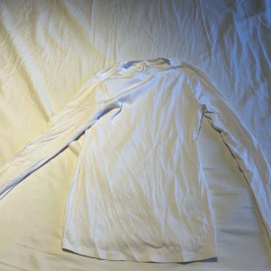 Vit långärmad tröja från H&M - En enkel och stilren vit långärmad tröja från H&M. Tröjan har rund halsringning och är tillverkad i mjuk bomull, perfekt för lager-på-lager eller som basplagg. Passar dig som gillar en clean och klassisk look.