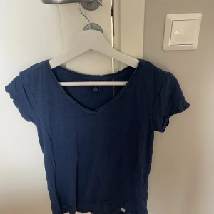 Marinblå t-shirt från U.S. Polo Assn. - En enkel marinblå t-shirt från U.S. Polo Assn. i 100% viskos. T-shirten har v-ringning och korta ärmar, perfekt för en avslappnad stil. Skön och lätt i materialet, passar till jeans eller shorts.