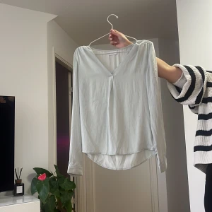 Vit v-ringad blus med långa ärmar - Säljer en stilren vit blus med v-ringning och långa ärmar. Blusen har en lätt och luftig känsla, perfekt för en clean och enkel look. Rundad nederkant ger en snygg siluett. Passar till både jeans och kjol.