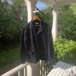 Blå manchester overshirt från East West - Snygg blå overshirt från East West i manchester. Jackan är i storlek L och har klassisk krage, tre stora fickor framtill och knäppning. 