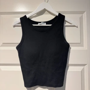 Svart ribbad linnetopp från Primark - En svart, ribbad linnetopp från Primark med rund halsringning och ärmlös design. Toppen är i stretchig bomull och har en croppad passform som sitter snyggt till både jeans och kjol. Inbyggda ilägg så ingen bh behövs.  Perfekt för en enkel och clean look.