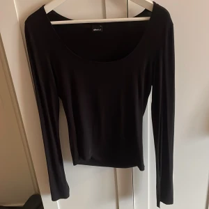 Svart långärmad topp från Gina Tricot - En svart långärmad topp från Gina Tricot med rundad, djup urringning. Toppens material är mjukt och stretchigt, perfekt för en enkel och stilren look. Ärmarna har en liten slitsdetalj vid mudden . Använd fåtal gånger 