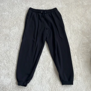 Svarta mjukisbyxor från lager 157, storlek M - Svarta mjukisbyxor från lager 157 med resår och snörning i midjan. Byxorna har muddar vid bensluten och är gjorda i mjukt material som är borstat på insidan för extra komfort. 