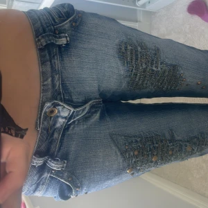 Miss co co blå jeans med nitar - Snygga blå jeans från Miss co co med slitna detaljer och coola nitar längs benen. Låg midja och klassisk femficksmodell. Jeansen har broderad logga på insidan av linningen och en lätt bootcut passform. Perfekta för dig som gillar en edgy stil. Jag är 168 och dom passar super bra på mig